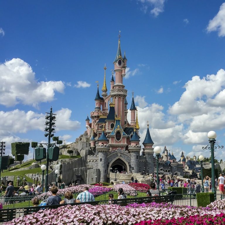 Disneyland Paris Schloss mit bunten Blumenbeeten und vielen Besuchern unter einem blauen Himmel.